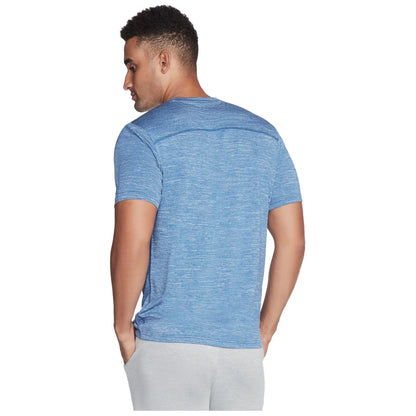 A man stands with his back to the viewer wearing a blue athletic shirt and light gray pants his hands are placed in the pockets of his pants