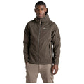 A young man stands confidently in a lightweight brown jacket with a hood showing off a stylish design and logo while wearing light-colored pants in a neutral background.