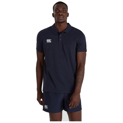 A man stands straight wearing a navy polo shirt and matching shorts with the logo of Canterbury visible on both garments against a plain white background.