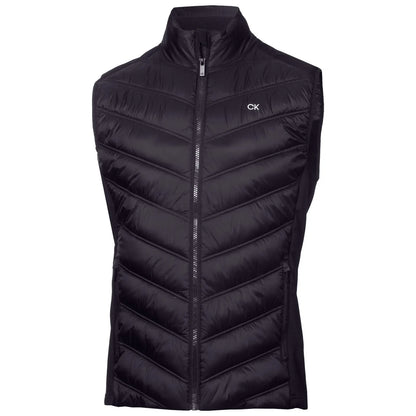 A black puffy vest with a high collar is displayed upright featuring a chevron pattern and a front zipper showcasing a small CK logo on the left chest area.