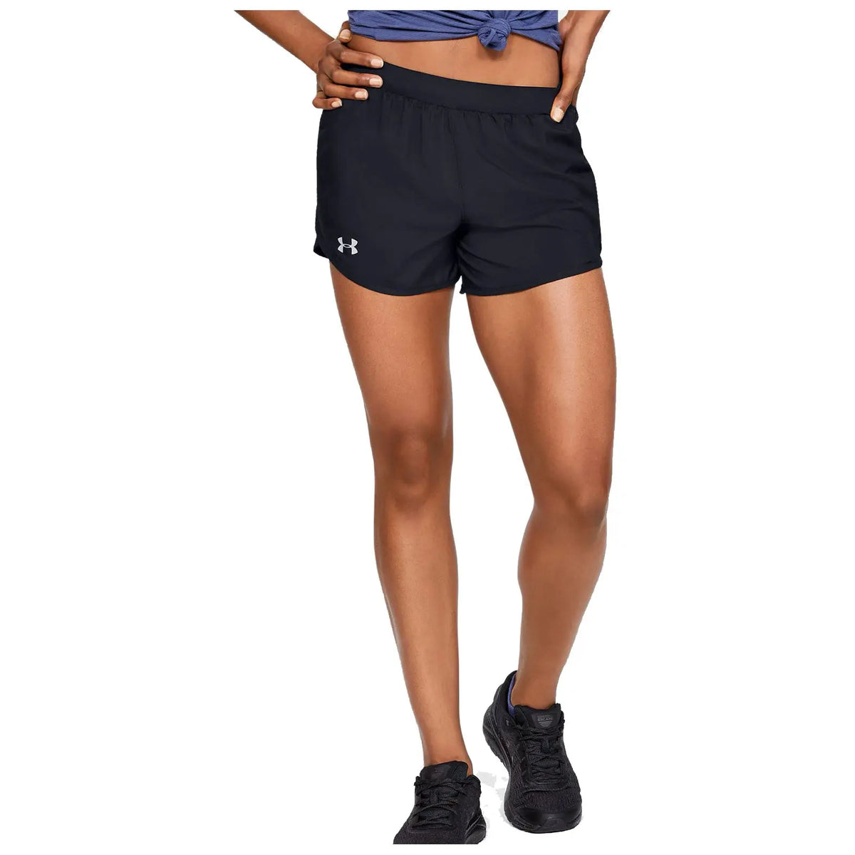A person stands confidently wearing black athletic shorts and a blue top with a knotted hem holding their hands on their hips against a plain white background.