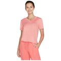 A woman stands wearing a pink v-neck t-shirt and matching drawstring pants smiling confidently while posing in a neutral background that emphasizes her casual style and comfort.