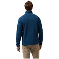 A man is wearing a blue fleece pullover with a high collar facing away from the viewer in a neutral background suggesting an outdoor or casual setting.