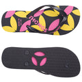 A pair of black flip-flops is displayed with a colorful floral pattern of pink and yellow petals on top and a textured black underside featuring two circular holes and two round pegs.