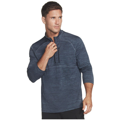 A man in a blue athletic pullover is adjusting the zipper while looking slightly off to the side, set against a plain background that emphasizes his casual attire.