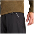 A close-up view of a person's torso wearing a brown sweater and black pants with a visible pocket featuring the logo Craghoppers, as a hand touches the fabric.
