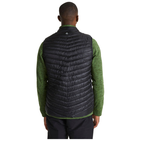 A person wearing a black puffy vest over a green long-sleeve shirt stands with their back facing the viewer in a neutral background, suggesting an outdoor or casual context.