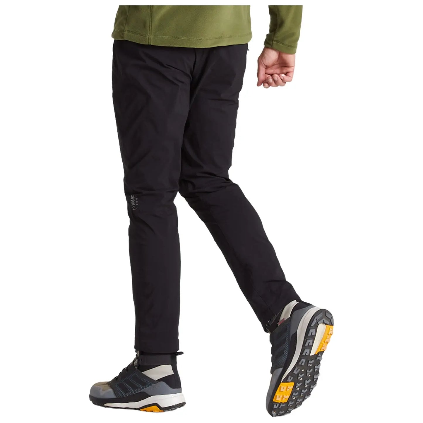 A person is walking, wearing black pants and gray athletic shoes with yellow accents, set against a neutral background, suggesting an active or outdoor context.