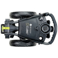 A compact black golf push cart with two large wheels is positioned upside down revealing its handle and controls designed for easy maneuvering in various terrains.