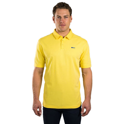A man stands confidently wearing a bright yellow polo shirt with a small blue logo on the left chest area against a plain white background. He has short hair and a neutral expression.