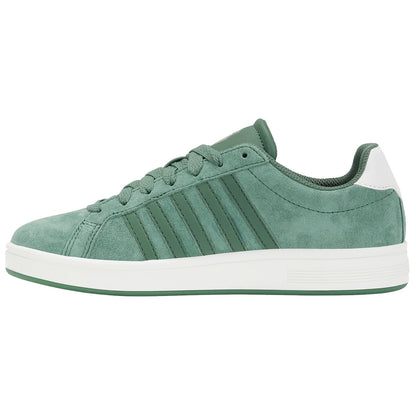 A green suede sneaker sits upright displaying six lace holes and three vertical stripes on its side while featuring a white heel cap in a neutral background.