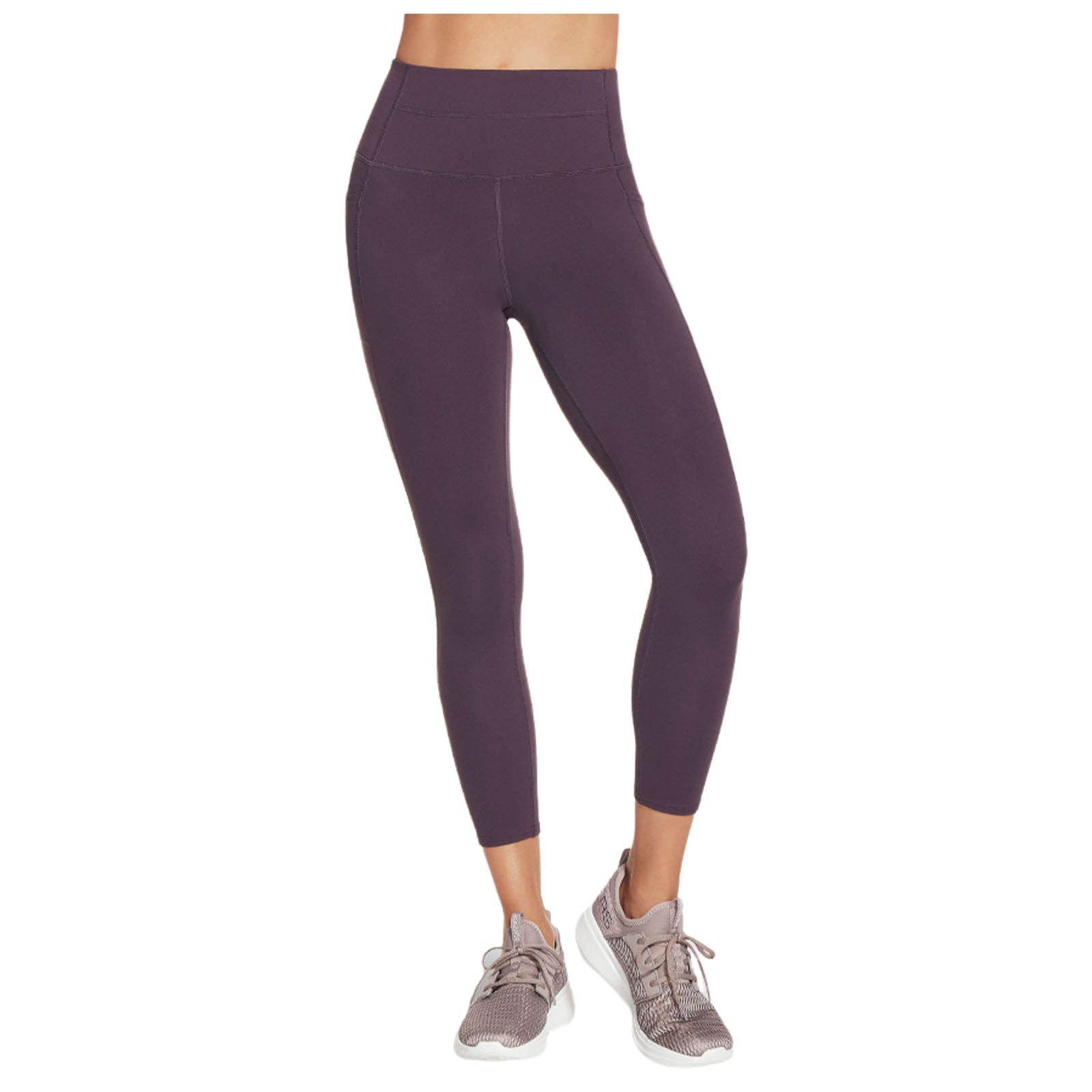 A pair of high-waisted purple leggings is displayed worn by a person standing in athletic shoes leading to an active or workout context. The background is plain.