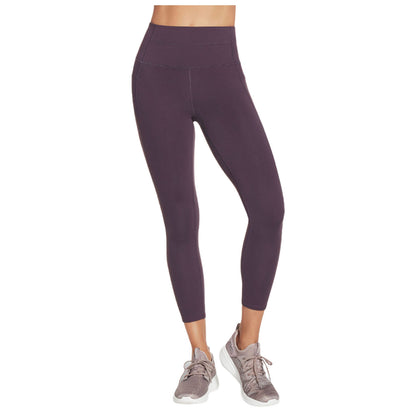 A pair of high-waisted purple leggings is displayed worn by a person standing in athletic shoes leading to an active or workout context. The background is plain.