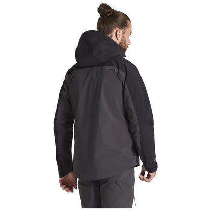 A person with long hair tied in a bun is wearing a black outdoor jacket with a hood facing away while standing in a neutral setting with a plain background.