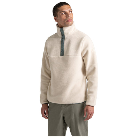 A man wearing a light beige fleece pullover with a high collar and buttoned front stands and looks upwards, set against a plain white background. He appears thoughtful and relaxed.