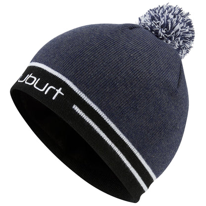 A dark blue knitted beanie hat with a white pompom sits at an angle showing its soft texture and contrasting black and white stripes along the brim adorned with the brand name.
