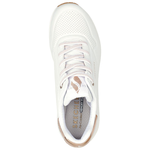A white sneaker with perforated details and light laces sits upright showcasing the cushioned insole embossed with Skechers branding and a tan accent at the heel