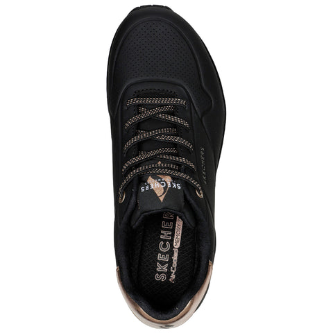 A black sneaker with perforated design and bronze accents sits against a plain background showcasing a sleek silhouette and thick laces highlighting its sporty appearance and cushioning features