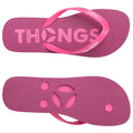 A pair of pink flip-flops are displayed showing the sole and straps with the word THONGS prominently printed on the footbed in a textured design suitable for casual wear.