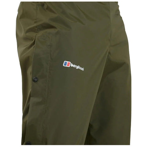An olive green waterproof pant is displayed featuring a logo from the brand Berghaus on the front side and snap closures along the side for secure fastening.