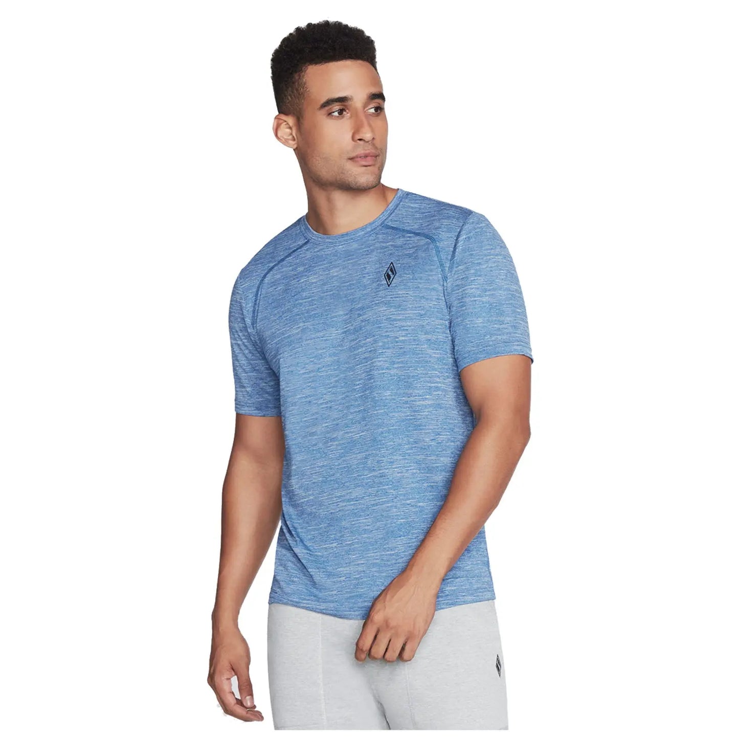 A man wearing a blue athletic t-shirt stands with a slight turn, looking to his left, against a plain white background, suggesting a promotional or advertising setting.