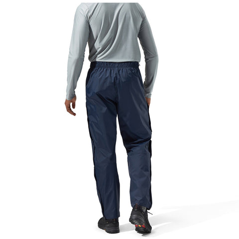 A person is standing with their back facing the viewer wearing navy waterproof pants and a light gray long-sleeve shirt in an indoor setting with a bright background.
