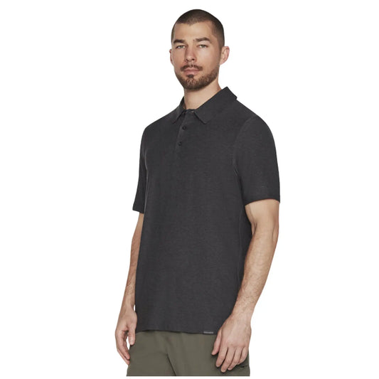 A man stands confidently wearing a dark gray short-sleeved polo shirt paired with olive green pants in a neutral background, posing with a serious expression.
