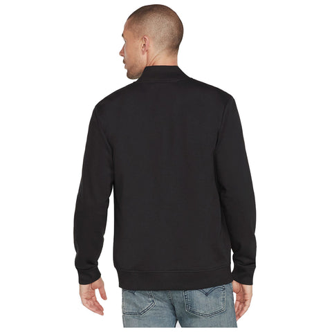 A man is standing with his back facing the viewer wearing a black sweatshirt and blue jeans in a neutral, undefined environment.