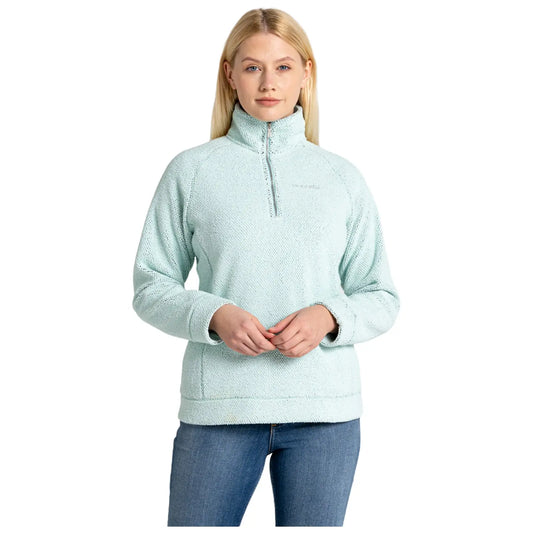 A woman is standing and smiling while wearing a light blue fleece pullover with a quarter zip in a casual indoor setting with a simple backgroundA woman is standing and smiling while wearing a light blue fleece pullover with a quarter zip in a casual indoor setting with a simple background