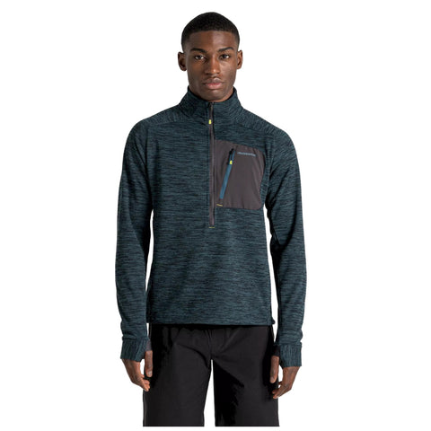 A young man is standing confidently while wearing a dark blue fleece pullover with a zippered collar and a black chest pocket appearing against a plain white background.
