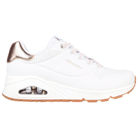 A white sneaker with a shiny gold accent on the heel features a lace-up design and a cushioned sole with an air pocket for comfort in casual or athletic use.