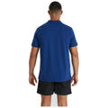 A person is standing with their back facing the viewer wearing a blue polo shirt and black shorts in a simple, unobtrusive setting that emphasizes their attire.