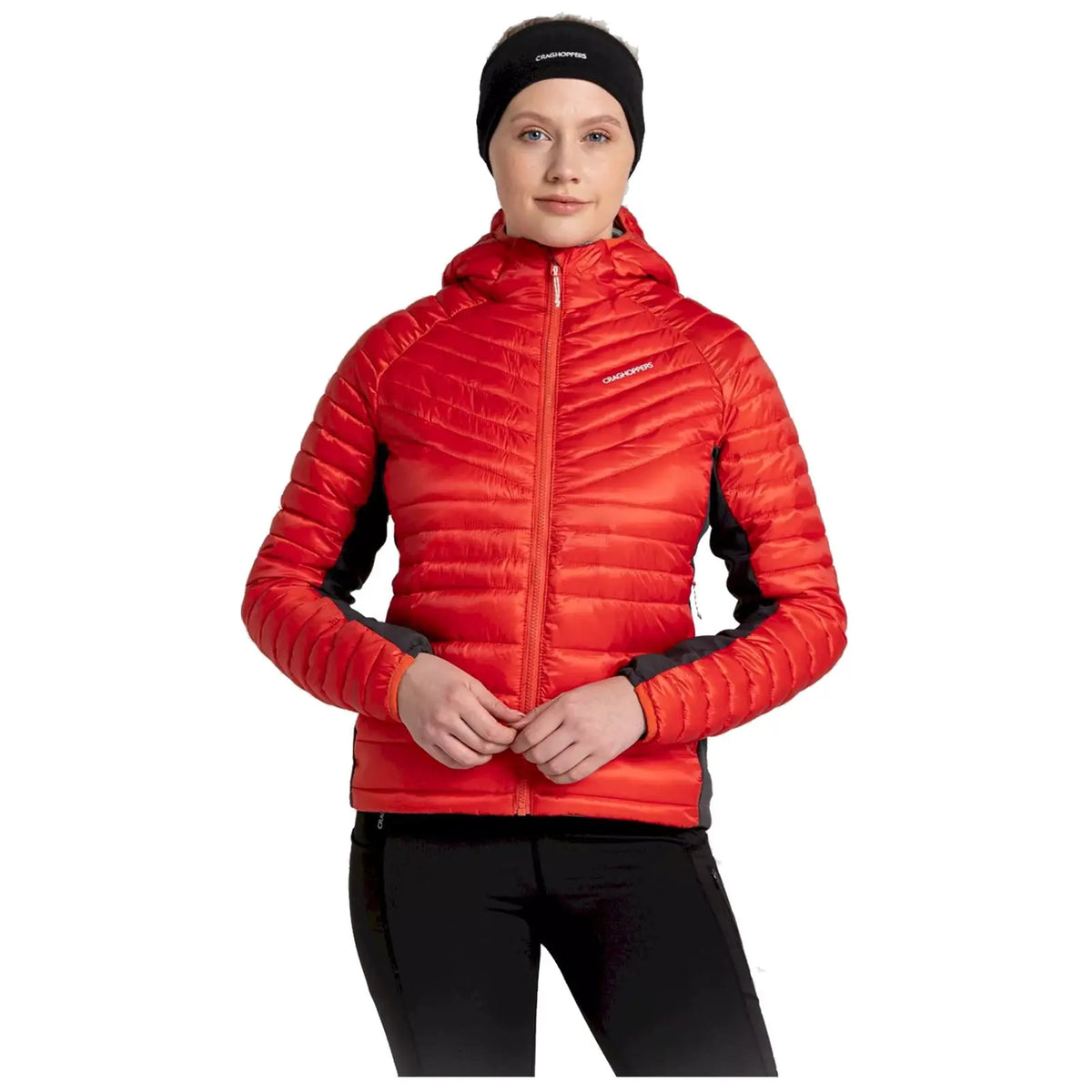 A person is wearing a red insulated jacket with a hood and black sleeves while holding their hands near the zipper in a plain background suitable for modeling or showcasing clothing.
