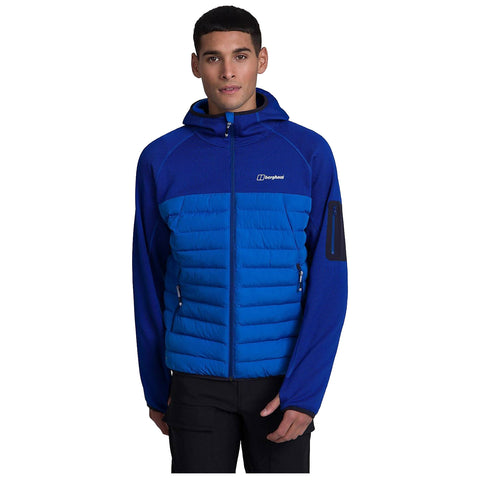 A young man is wearing a blue jacket with a puffy lower section and textured upper sleeves. He is standing against a plain background looking directly at the viewer.
