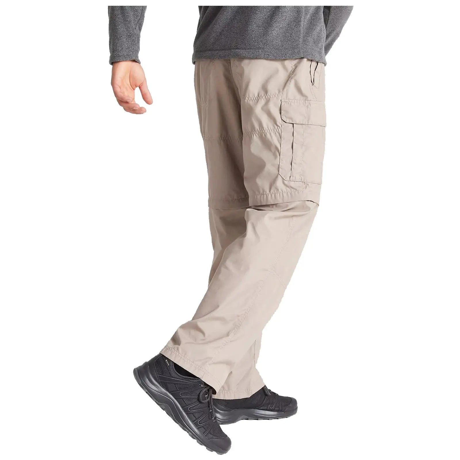 A person is walking in light-colored cargo pants and black athletic shoes with a gray long-sleeve shirt in a neutral environment. The focus is on their lower body and footwear.