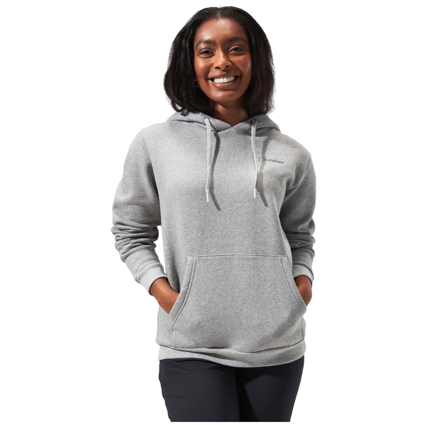 A woman wearing a gray hoodie stands smiling with her hands in the front pockets against a plain background, exuding a casual and friendly demeanor.