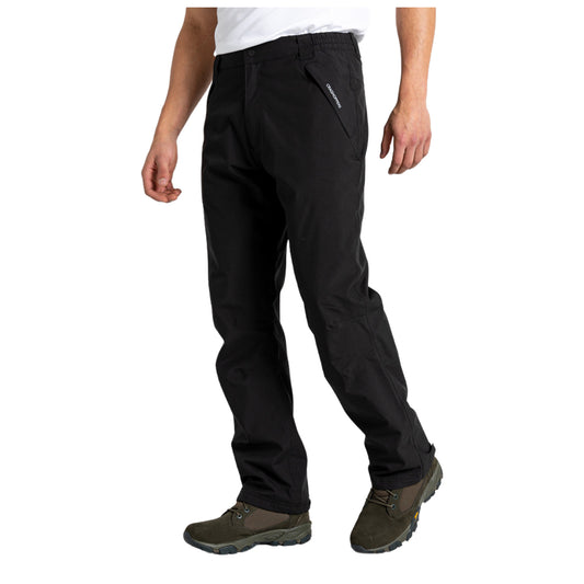 Black technical pants are being worn by a person standing with one hand on their hip while wearing green hiking shoes in a neutral background environment.