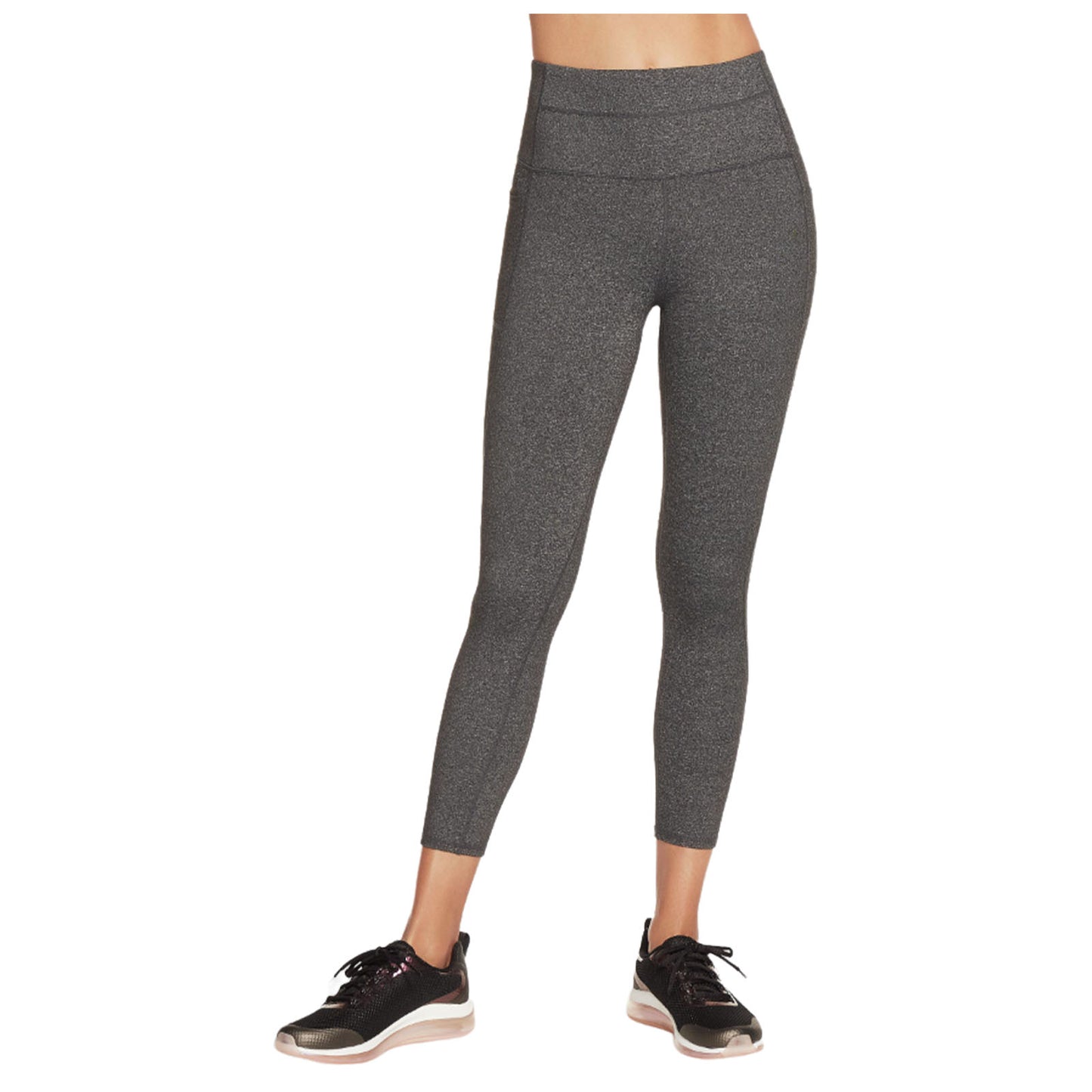 A pair of dark gray leggings hug a figure's legs and hips while a person stands in athletic shoes on a neutral background, suggesting a focus on fitness or casual wear.
