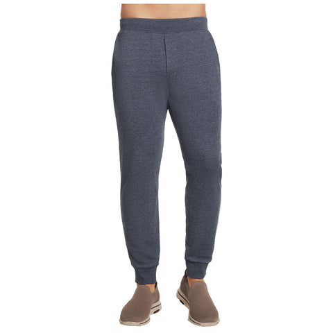 Gray jogger pants are displayed standing upright with an elastic waistband and fitted cuffs. They are worn with light brown slip-on shoes in a neutral environment.