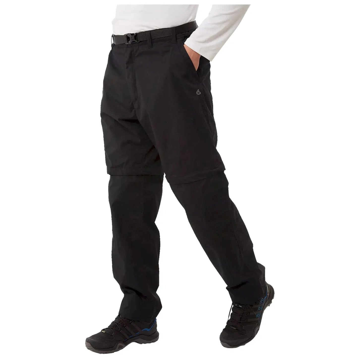 Black convertible pants are being worn by a person with one hand in a pocket while standing on a flat surface dressed in a long-sleeve white shirt and black shoes.