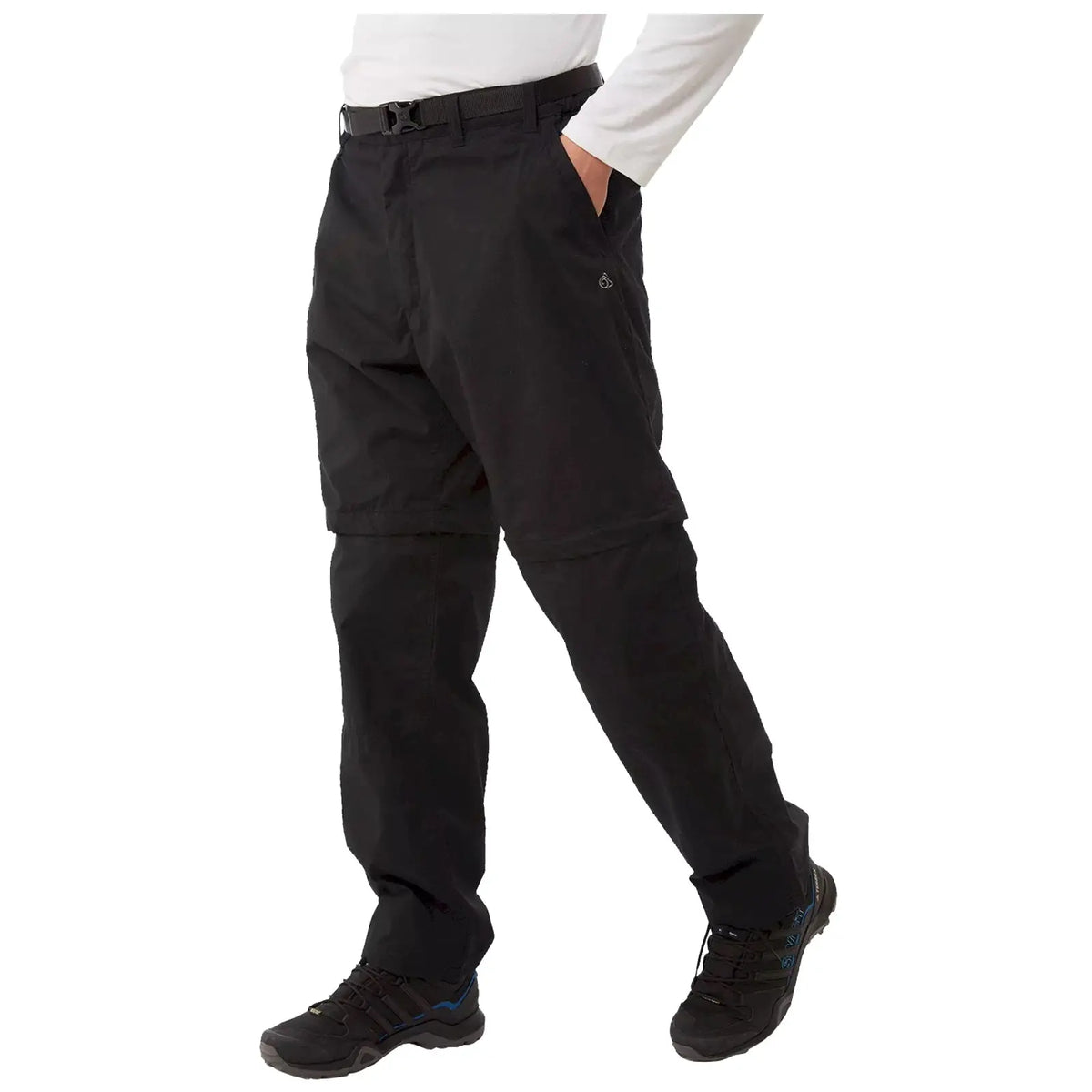 Black convertible pants are being worn by a person with one hand in a pocket while standing on a flat surface dressed in a long-sleeve white shirt and black shoes.