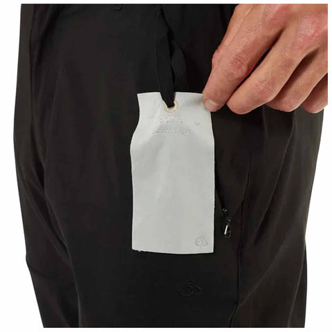 A hand holds a white tag labeled "G-SHOCK" and "Wipes" positioned inside the pocket of black pants showcasing a simple, functional design in a neutral environment.