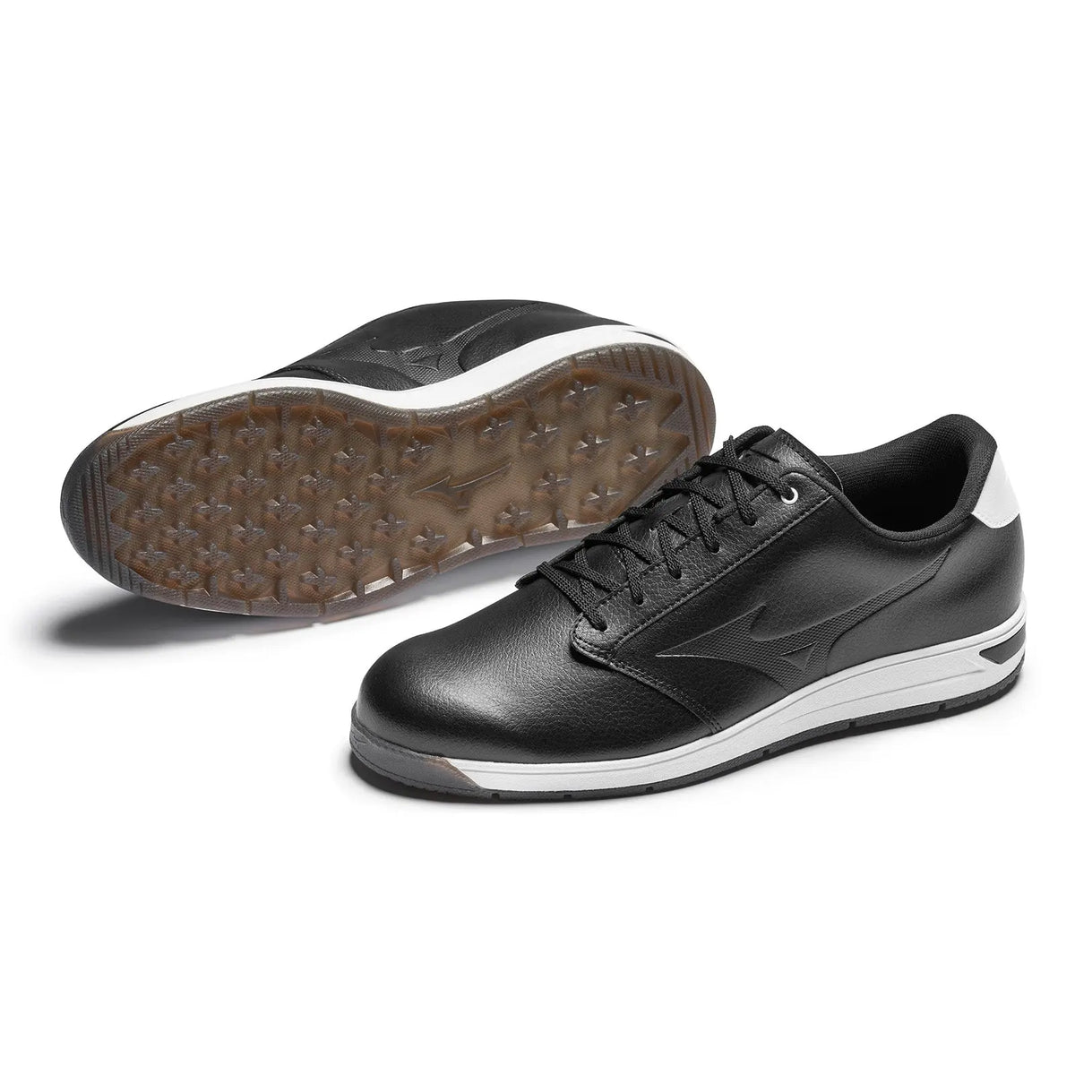 Black athletic shoes with a textured rubber sole are displayed on a white background one shoe upside down revealing the sole while the other is positioned upright showing the side view.