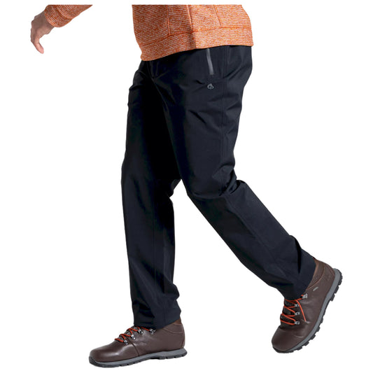 A person is walking with their left leg lifted while wearing black pants and brown hiking shoes. The environment is neutral and uncluttered, focusing on the individual’s movement and attire.