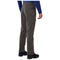 A person stands with their back to the viewer wearing gray pants and black shoes while their left hand is slightly raised in an outdoor or casual setting.