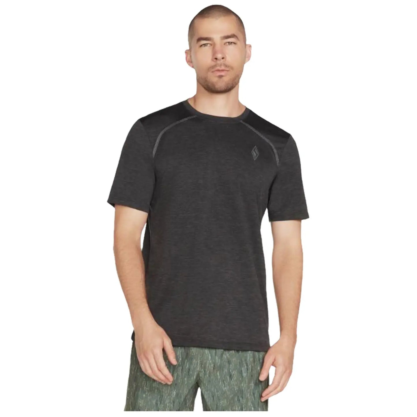 A man stands wearing a short-sleeve black athletic shirt and patterned green shorts with a neutral expression against a plain white background. He appears ready for exercise or casual wear.