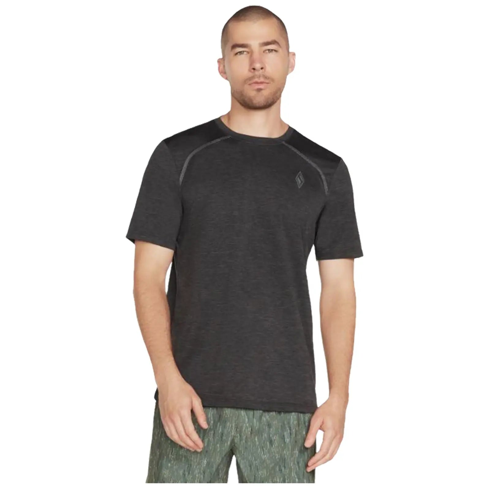 A man stands wearing a short-sleeve black athletic shirt and patterned green shorts with a neutral expression against a plain white background. He appears ready for exercise or casual wear.