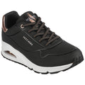A black athletic shoe with a sleek design features a textured upper and bronze accents while resting on a flat surface showcasing its sole and perforated details.