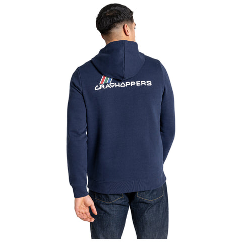 A person wearing a navy blue hoodie stands facing away showing the back design that includes the word CRAGHOPPERS and colorful stripes above it in a casual indoor setting.