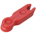 A red plastic tool sits on a flat surface designed to hold two small circular objects it has a forked end for gripping or lifting items in close proximity.